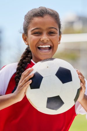 Soccer, sports and happy Indian girl athlete holding a sport ball on a school field. Portrait of fitness, football and exercise of a child smile excited about training, workout and game motivation